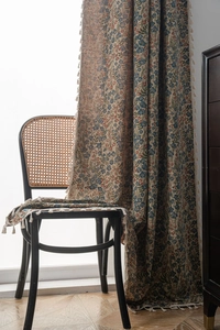 Detail of floral pattern curtain with tassel edges on a vintage wicker chair