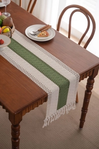 Dettaglio del runner da tavola intrecciato verde e bianco con nappe su tavolo in legno