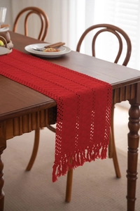 Dettaglio di un runner da tavola all'uncinetto rosso con nappe e trama a maglia traforata