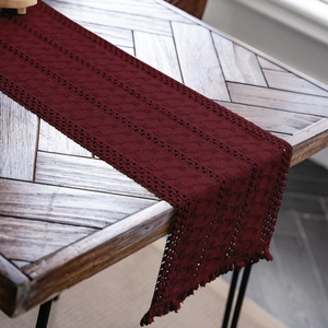 Dettaglio del runner da tavola rosso scuro intrecciato con pizzo e nappe su legno