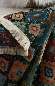 Detail of bohemian jacquard sofa throw with green diamond patterns and white cotton tassels