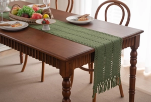 Dettaglio runner da tavola verde scuro all'uncinetto con trama traforata e nappe