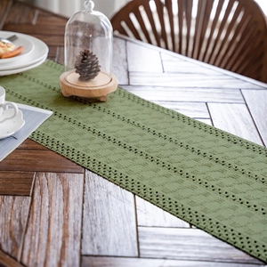 Dettaglio del runner da tavola verde oliva con trafori geometrici su legno naturale