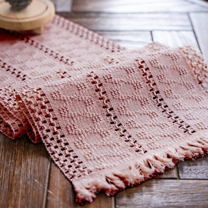 Dettaglio del runner da tavola rosa all'uncinetto con motivi geometrici e nappe