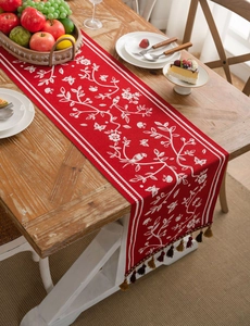 Red table runner featuring white jacquard bird and floral patterns with tassel details