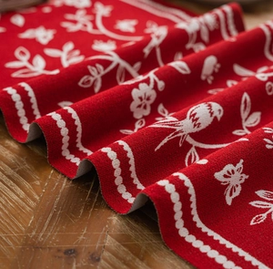 Detail of red table runner with white floral bird jacquard pattern on wood surface