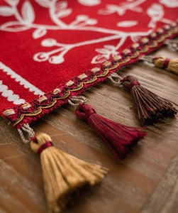 Close-up of red jacquard table runner with white embroidery and colorful silk tassels