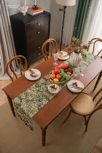 Detailed close-up of green floral table runner with elegant tassels on a wooden table