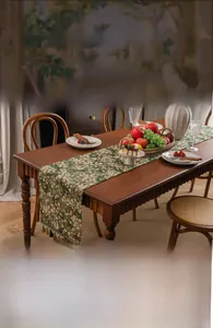 Detail of vintage green floral table runner with elegant tassels on dark wood table