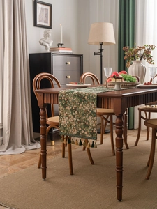 Close-up of green floral jacquard table runner with decorative tassels on wood table