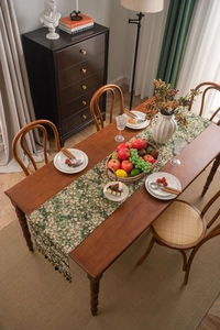 Detailed view of green floral table runner with elegant fringe tassels in a rustic setting