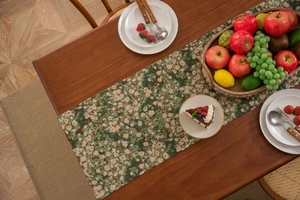 Detailed top view of a green floral table runner with tassels on a wooden dining table
