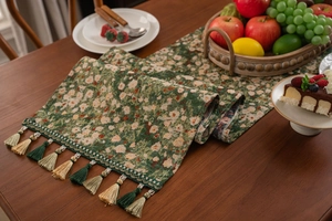Close-up of green jacquard table runner with fringe on walnut dining table