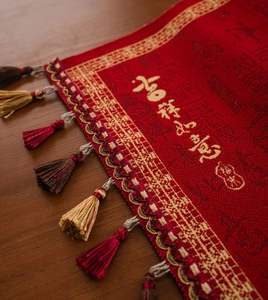 Detail van rode Chinese tafelloper met gouden borduursels en decoratieve kwastjes