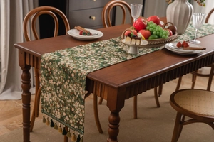 Detail of green floral jacquard table runner with decorative fringe on a wooden table