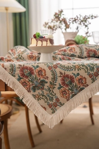 Detailed view of vintage jacquard tablecloth with floral patterns and ivory fringe tassels