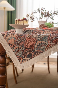 Detail of bohemian jacquard tablecloth featuring orange fan patterns and long fringe tassels