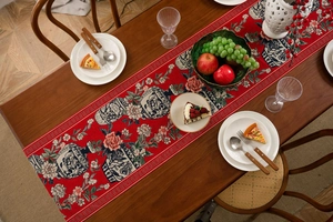 Detail of red jacquard table runner with peony and porcelain motifs on wooden table