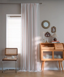 Close-up of beige cotton linen curtain with red vertical stripes and white fringe trim