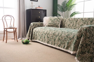 Detailed view of dark green floral sofa cover with elegant fringe edges and matching pillow