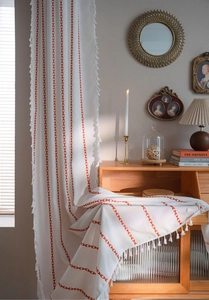 Detail of white linen curtain with red V-shaped embroidery and small white tassels