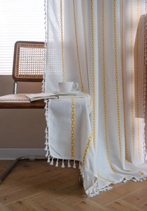 Detail of white cotton linen curtain with yellow geometric embroidery and tassel fringe