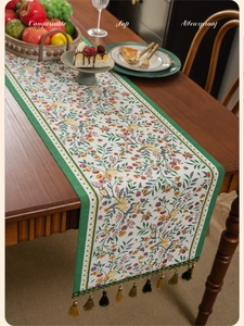 Close-up of green jacquard table runner with vintage floral pattern and tassel details