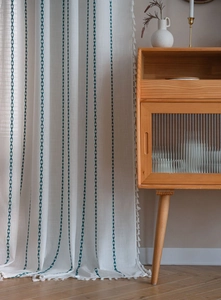 Détail d'un rideau crème avec rayures de feuilles vert foncé et bordure à pompons blancs