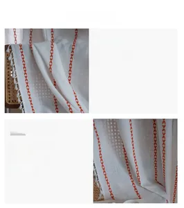 Macro shot of white linen curtain featuring orange geometric embroidery and soft fringe edge