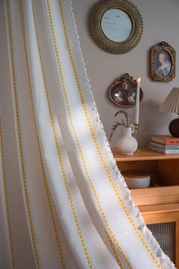 Detailed close-up of bohemian curtain with yellow leaf pattern and white tassel trim