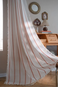 Detail of bohemian white curtain with red vertical embroidery and decorative tassels