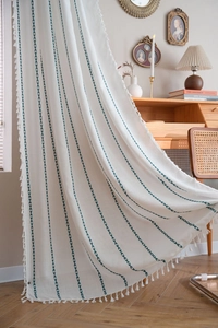 Détail du rideau en lin crème avec broderie verte ondulée et décor de pompons blancs