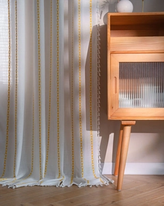 Detail of white linen curtain with yellow geometric diamond stripes and white tassel trim