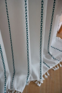 Vue détaillée d'un rideau blanc avec broderie de feuilles sarcelle et glands à franges