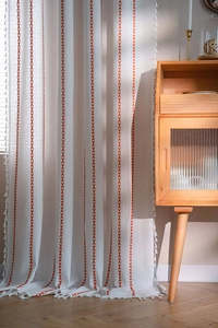 Close-up of bohemian linen curtain with red geometric embroidery and cotton tassels
