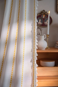 Detail of minimalist cream linen curtain with yellow leaf embroidery and white tassels