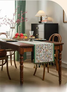 Detail of green floral jacquard table runner with golden fringe tassels on a wooden table