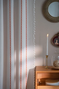 Close-up of white linen curtain with red arrow stripes and white tassel ball trim decor