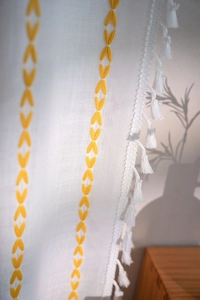 Detail of white cotton linen curtain with yellow V-shaped embroidery and white fringe tassels