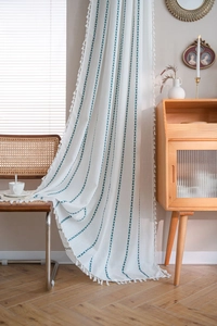 Détail d'un rideau blanc en coton et lin avec rayures brodées bleues et pompons latéraux