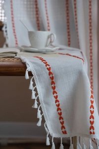 Close-up of white cotton linen table runner with orange heart embroidery and fringe details