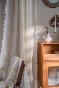 Detail of ivory cotton linen curtain with yellow geometric embroidery and white tassels