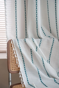 Détail du rideau en lin bohème avec broderie fléchée sarcelle et pompons blancs faits main