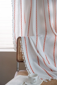 Detail of Nordic white linen curtain with red V-shaped embroidery and delicate tassel edges