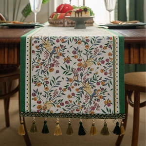 Detail of green jacquard table runner with colorful flower bird patterns and elegant tassels