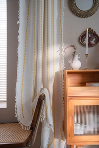 Detail of bohemian cream cotton curtain with yellow embroidery and white tassels on a chair