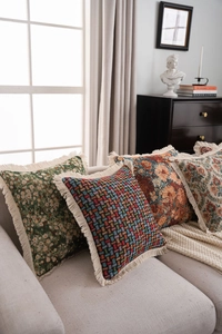 Detail of vintage jacquard throw pillows with fringe trim on a grey fabric sofa