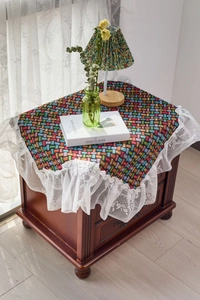 Close-up of a colorful woven tablecloth featuring elegant white lace edges on a wooden table