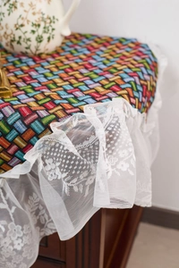 Detail of colorful geometric woven tablecloth featuring elegant white lace ruffled edges