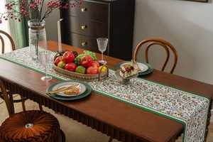 Detailed close-up of green jacquard table runner with floral bird patterns on a wooden table